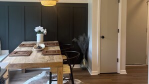 Un coin repas avec une table en bois, des sets de table en fibres tressées, un luminaire suspendu et un tapis en peau de vache.