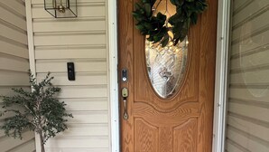 Une porte d’entrée en bois ornée d’une guirlande décorative, d’une plante en pot et d’un perron pavé de pierres.