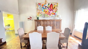 A dining area with a wooden table and chairs, a colorful painting above the table, and a kitchen sign in the background. - Large charming house with swimming pool, huge garden and close to state forest (Saint-Laurent)