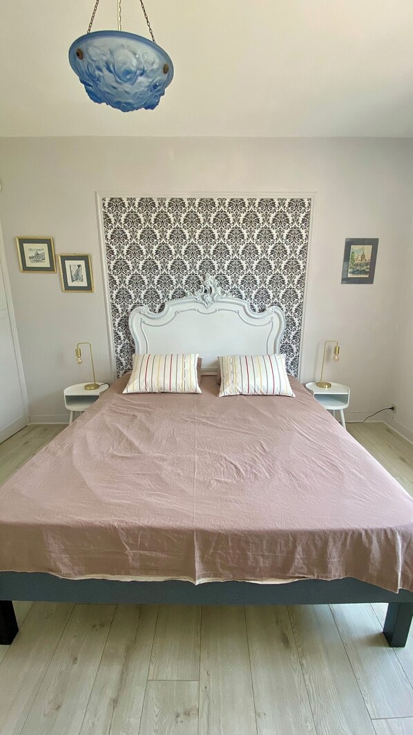 A bedroom with a large bed, two bedside lamps, a patterned headboard, and framed pictures on the wall. - Large charming house with swimming pool, huge garden and close to state forest (Saint-Laurent)