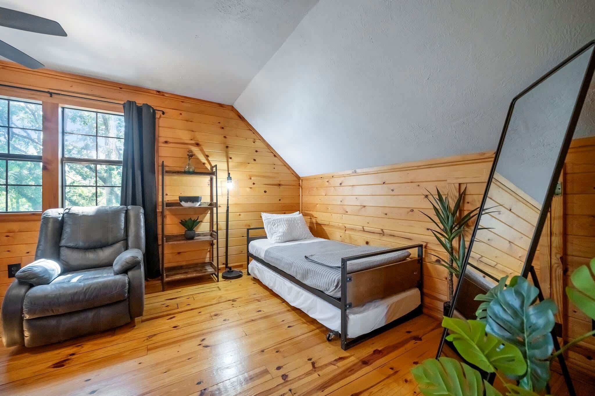 A cozy room with wooden walls, a bed, a chair, and a floor lamp.