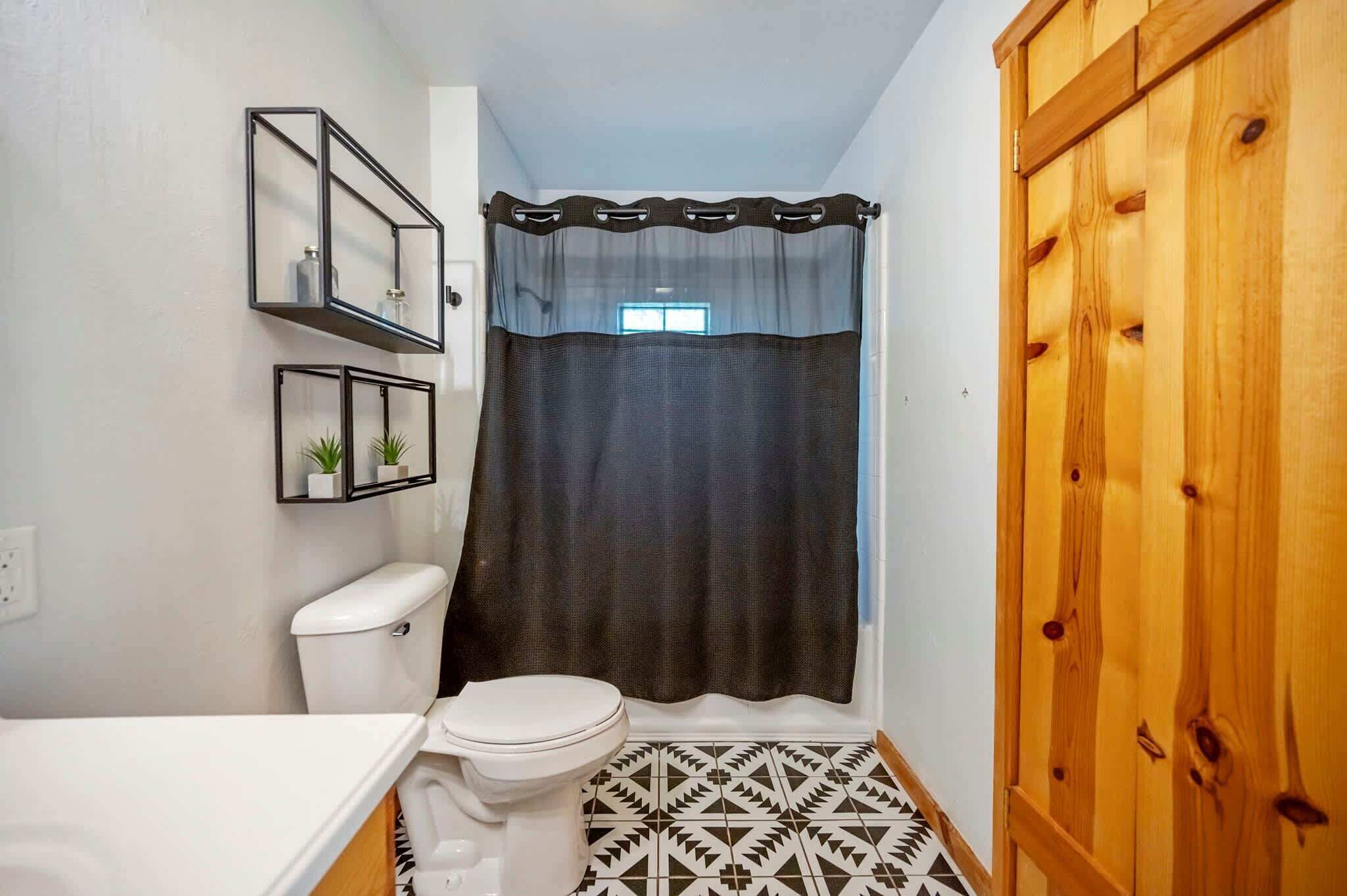 A bathroom with a toilet, a shower curtain, a wooden wardrobe, and a mirror with a shelf.