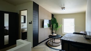 A modern living room with a large plant, a round table, and a TV mounted on the wall. - Aki Banda Suites (Willemstad)