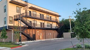 A multi-story building with a brick facade, a central staircase, and a flat roof. - Charming 2-Bedroom Apartment in Downtown Manor (Manor)