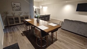 A modern dining area with a wooden table, bar stools, and a grey sofa. - Charming 2-Bedroom Apartment in Downtown Manor (Manor)