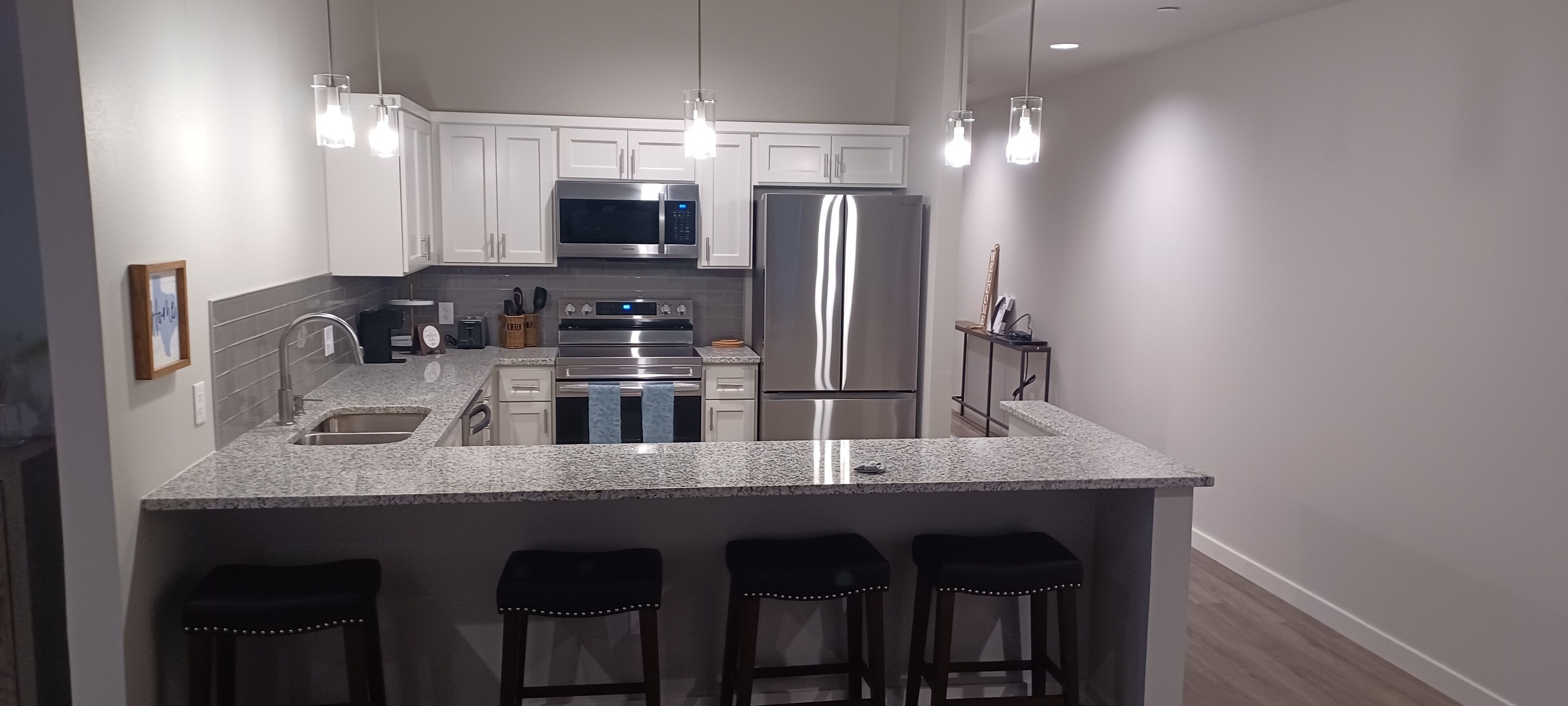 A modern kitchen with white cabinets, stainless steel appliances, granite countertops, and bar stools.