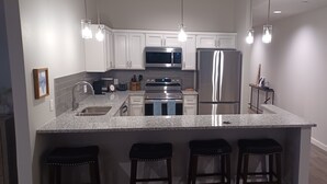 A modern kitchen with white cabinets, stainless steel appliances, granite countertops, and bar stools. - Charming 2-Bedroom Apartment in Downtown Manor (Manor)