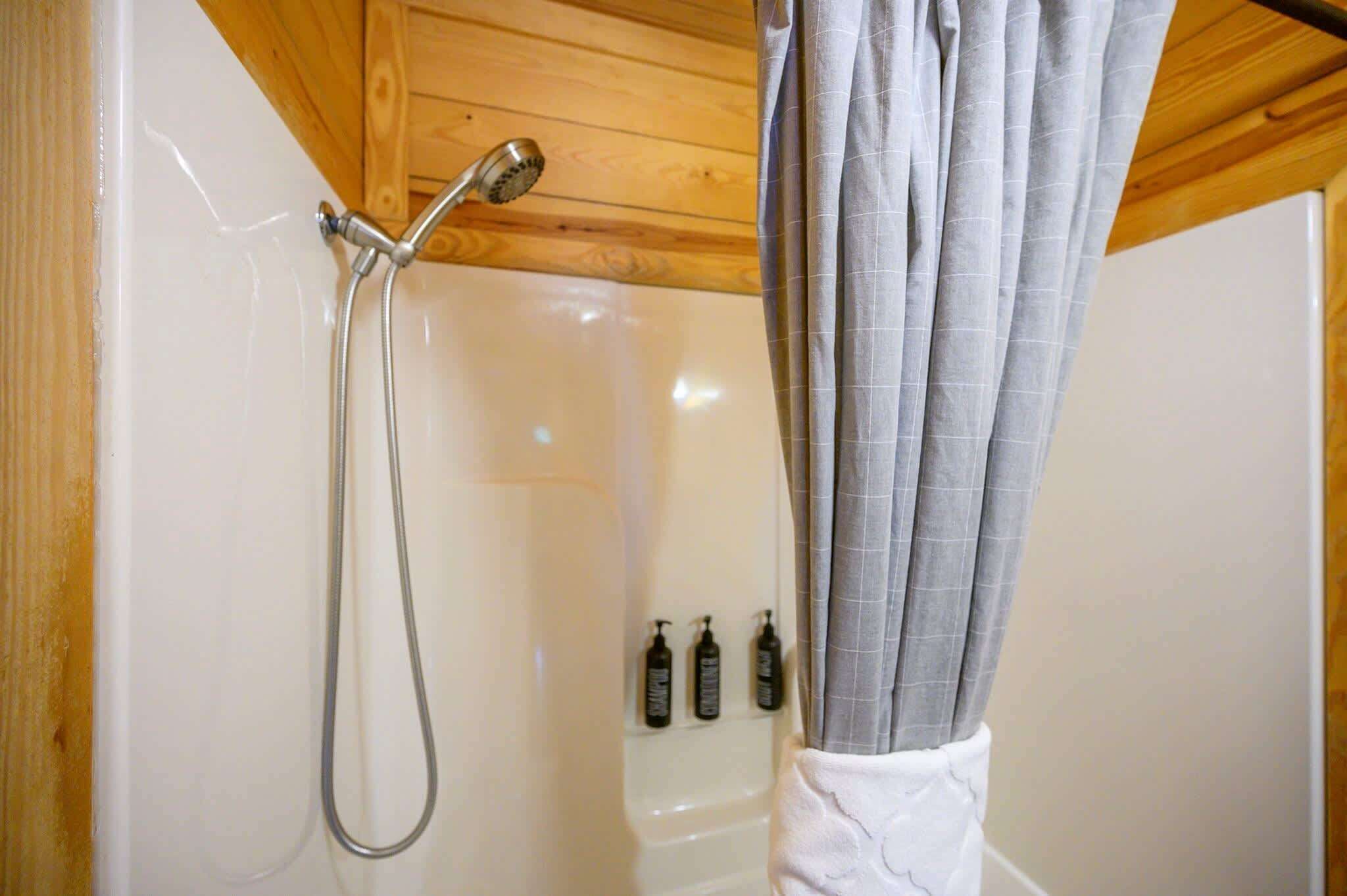 A shower area with a wooden ceiling, a showerhead, and a curtain.