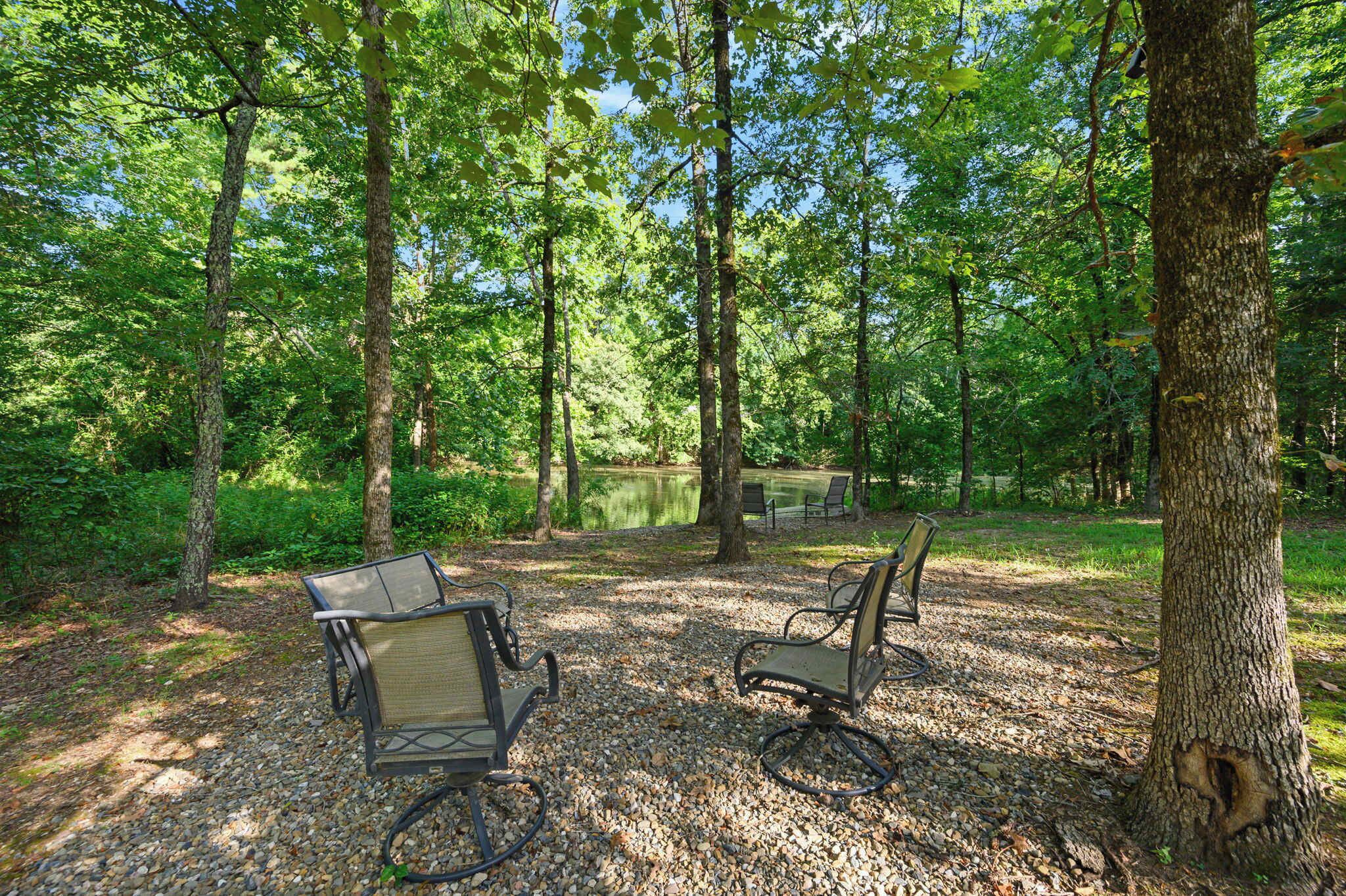 A serene outdoor seating area with two chairs and a table, surrounded by trees and a pond.