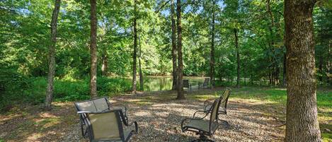 A serene outdoor seating area with two chairs and a table, surrounded by trees and a pond.