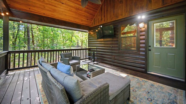 A covered porch with wicker furniture, a television, and a green door. - Sunset Ridge Cozy Cabin for 6 (Broken Bow)