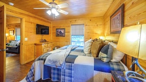 A cozy cabin room with a bed, a ceiling fan, a TV, and a window. - Sunset Ridge Cozy Cabin for 6 (Broken Bow)