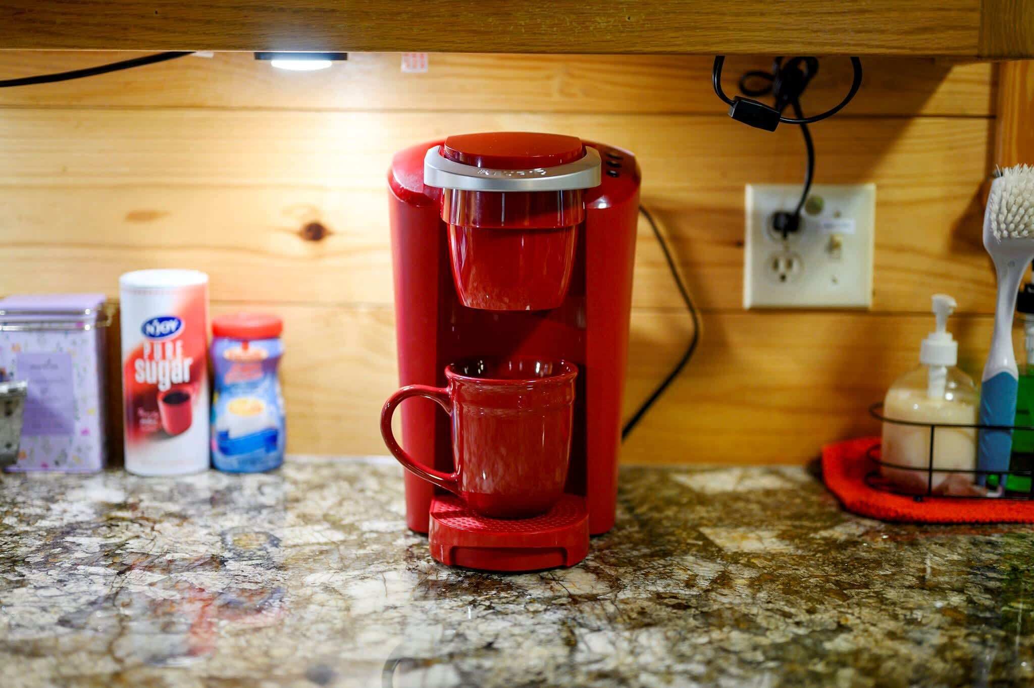 A red coffee maker on a granite countertop with a wooden cabinet in the background.