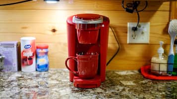 Una cafetera roja sobre una encimera de granito con un mueble de madera al fondo.