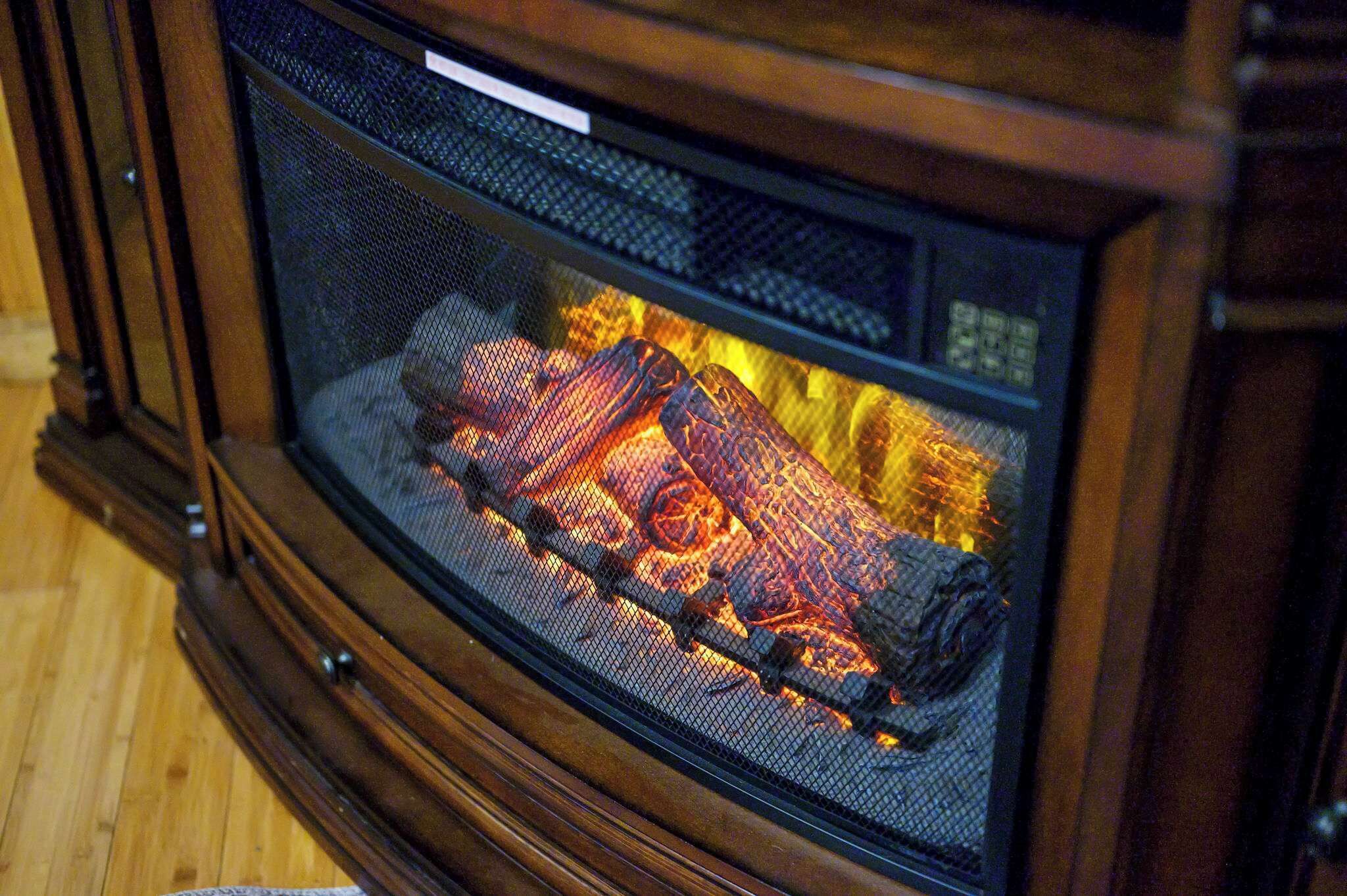 A fireplace with a metal screen, burning logs, and a wooden frame.