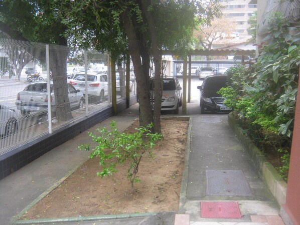 A narrow urban pathway with a dirt patch and a metal fence on one side, and a sidewalk on the other.