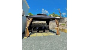 Un espacio de estar techado al aire libre con un muro de piedra de fondo y un cielo azul despejado.