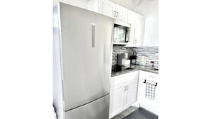 Una cocina moderna con armarios blancos, un refrigerador de acero inoxidable y un microondas.