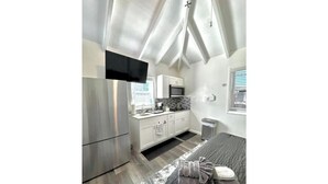 Une chambre moderne équipée d’un lit, d’un téléviseur à écran plat, d’une kitchenette et d’une grande fenêtre.