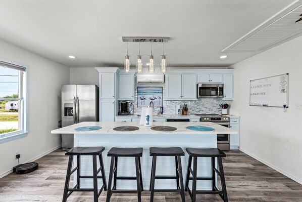 A modern kitchen with a central island, bar stools, stainless steel appliances, and a view of the outdoors. - Cozy Waterfront Getaway for 2! Green Fishing Light! Amazing Views! (Hitchcock)