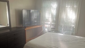 A bedroom with a bed, a dresser, a television, and a window with curtains. - Charming apartment in awesome Brooklyn. (Brooklyn)