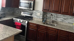 A modern kitchen with dark wooden cabinets, stainless steel appliances, granite countertops, and a red towel hanging on the oven. - Charming apartment in awesome Brooklyn. (Brooklyn)