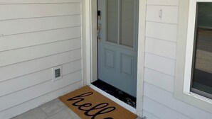 Eine weiße Tür mit der Nummer 102 darüber, eine Fußmatte mit dem Schriftzug "hello" und ein kleines Fenster zur Rechten.