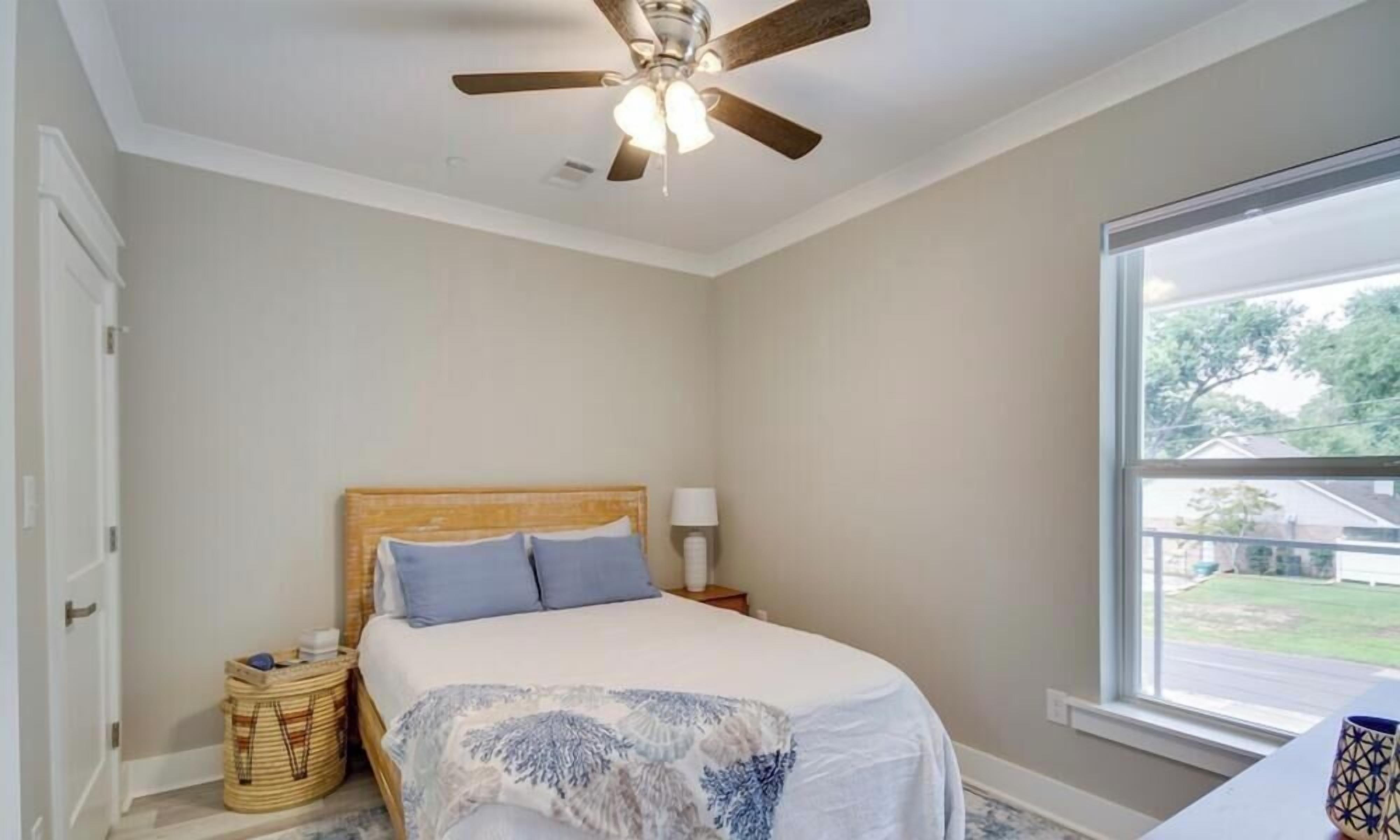 A bedroom with a bed, a ceiling fan, a window, and a view of the outside.