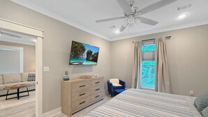 Un dormitorio con cama, televisor montado en la pared, ventilador de techo y ventana con cortinas.