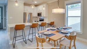 Una cocina moderna con armarios blancos, electrodomésticos de acero inoxidable y un comedor con mesa y sillas de madera.