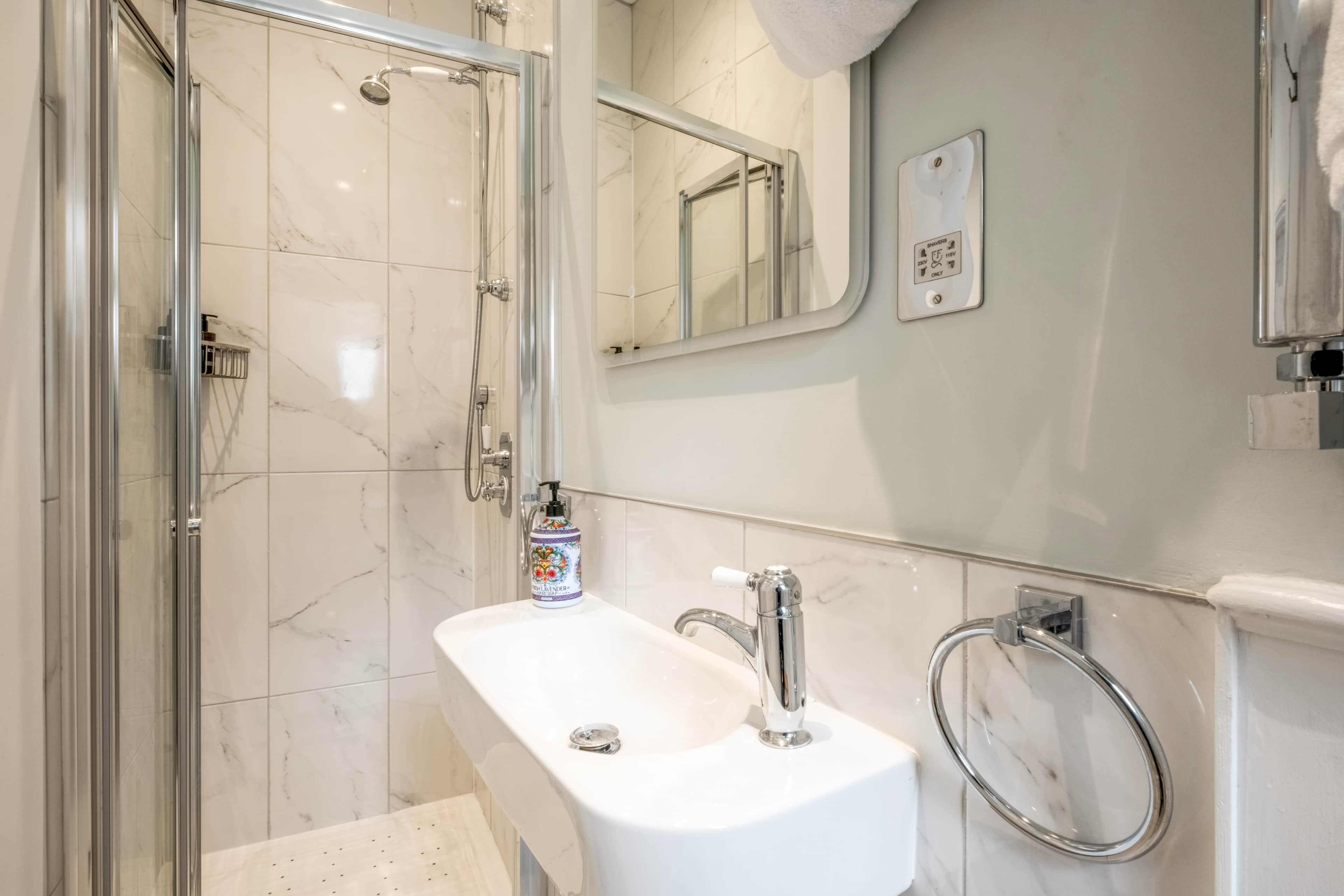 A bathroom with a glass shower enclosure, a white sink with chrome fixtures, and a towel ring.