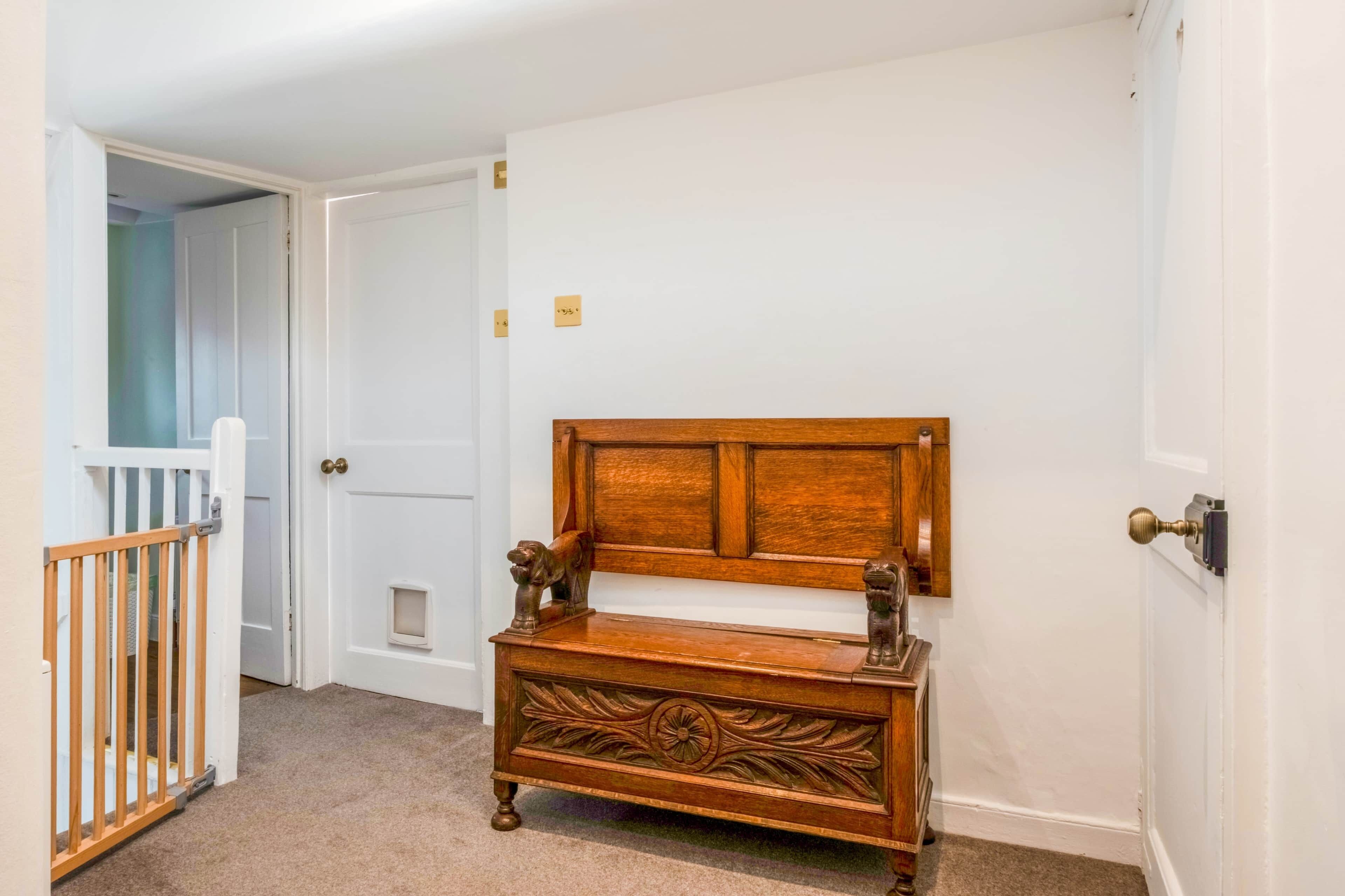 A hallway with a wooden bench, a baby gate, and a door with a brass doorknob.