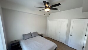 Un dormitorio con cama, mesita de noche, ventilador de techo y armario.