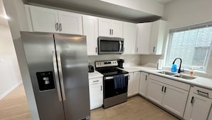 Una cocina moderna con armarios blancos, electrodomésticos de acero inoxidable y un ventanal con vistas a un edificio de ladrillo.