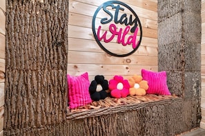 Una pared de madera con un letrero que dice 'Stay Wild' y un banco tejido con cojines de colores.