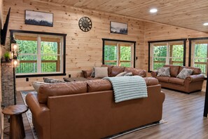 A spacious living room with wooden walls, large windows, and leather sofas. - Sleeps 12, 2 Kitchens, 2 Game Rooms, Hot Tub, Mountain Views, Near Dollywood (Pigeon Forge)
