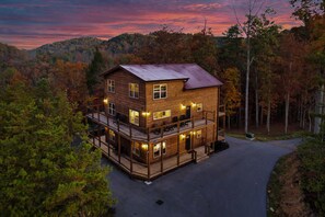 A two-story wooden cabin with a balcony, surrounded by a forested area. - Sleeps 12, 2 Kitchens, 2 Game Rooms, Hot Tub, Mountain Views, Near Dollywood (Pigeon Forge)