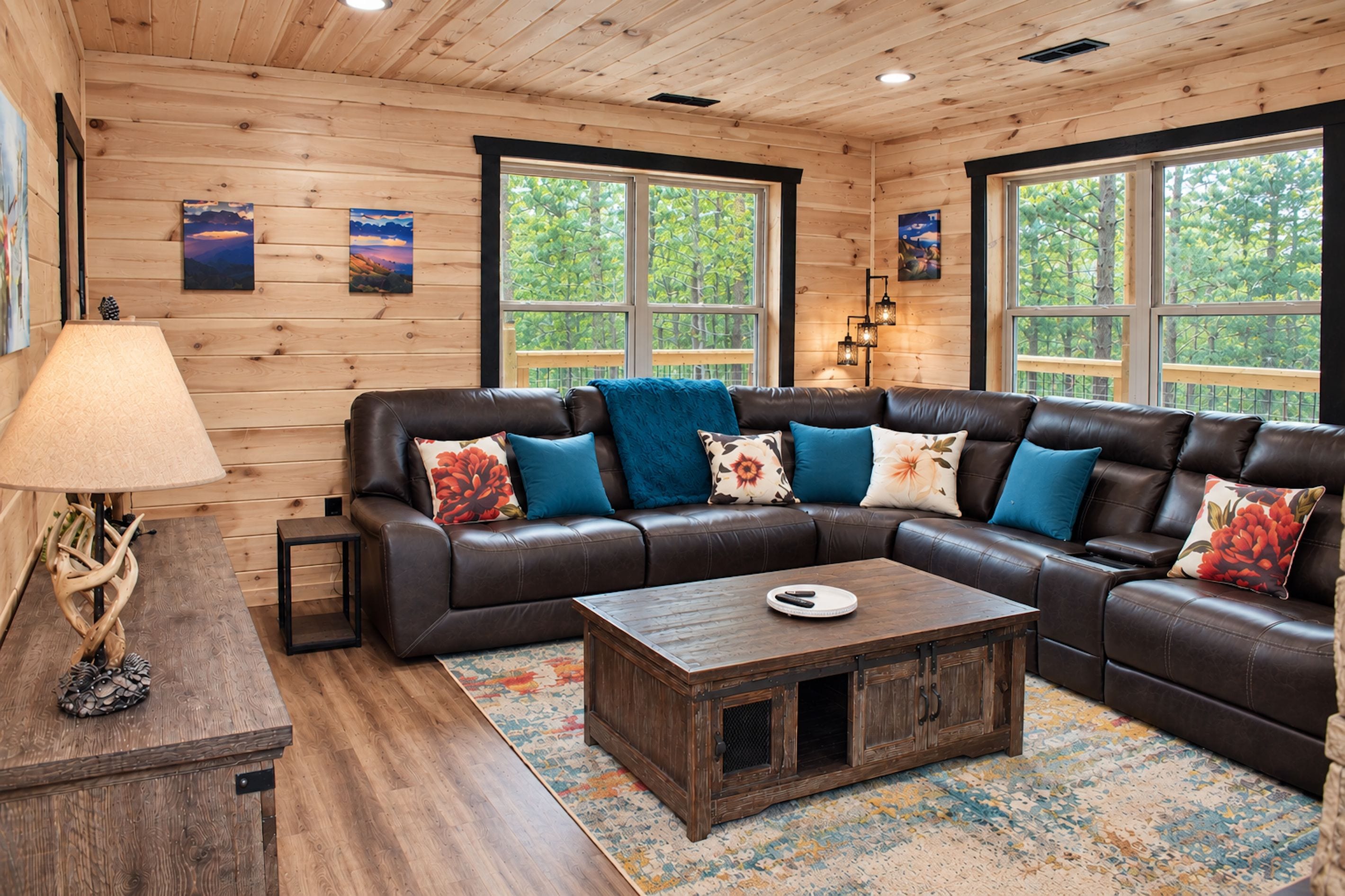 A cozy living room with a leather sectional sofa, a wooden coffee table, and a large window providing a view of trees.