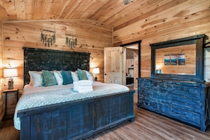 A wooden cabin bedroom with a bed, bedside lamps, a dresser, and a mirror.