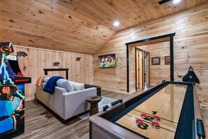 Une pièce chaleureuse avec un plafond en bois, un canapé, une table de baby-foot et un téléviseur diffusant un match de sport.