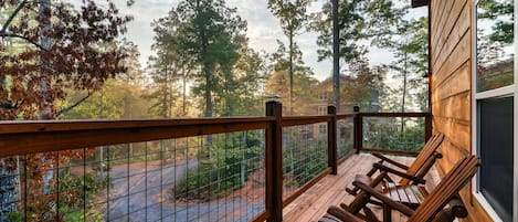 A wooden deck with a railing, two wooden chairs, and a view of a forested area.