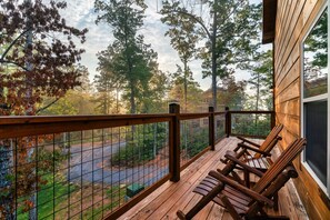 A wooden deck with a railing, two wooden chairs, and a view of a forested area.