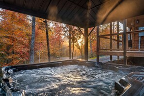 Un jacuzzi con vista a árboles otoñales y una terraza de madera.