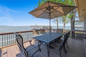 Eine Terrasse mit Tisch und Stühlen, mit Blick auf ein Gewässer, im Hintergrund ein Steg.