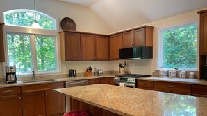 A kitchen with wooden cabinets, a granite countertop, a stove, and a large window. - 3 Bedroom house in Cotuit with screened porch and bay view (Barnstable)