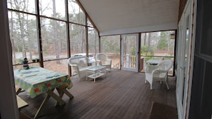 A covered patio with a table and chairs, large windows, and a view of trees. - 3 Bedroom house in Cotuit with screened porch and bay view (Barnstable)