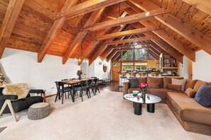 A spacious loft with exposed wooden beams, a dining area, and a cozy seating area with a coffee table. - 4BR Tahoe Cabin w/ Hot Tub, BBQ & Ping Pong Next to Lake & Paige Meadows Trails (Tahoe City)