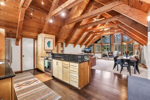 A spacious kitchen with wooden beams, a dining area with a table and chairs, and a view of the outdoors through large windows.