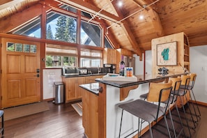 A kitchen with wooden cabinets, a central island, bar stools, and a large window. - 4BR Tahoe Cabin w/ Hot Tub, BBQ & Ping Pong Next to Lake & Paige Meadows Trails (Tahoe City)