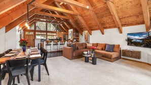 Un loft espacioso con techo alto, comedor, sala de estar con sofá y cocina al fondo.